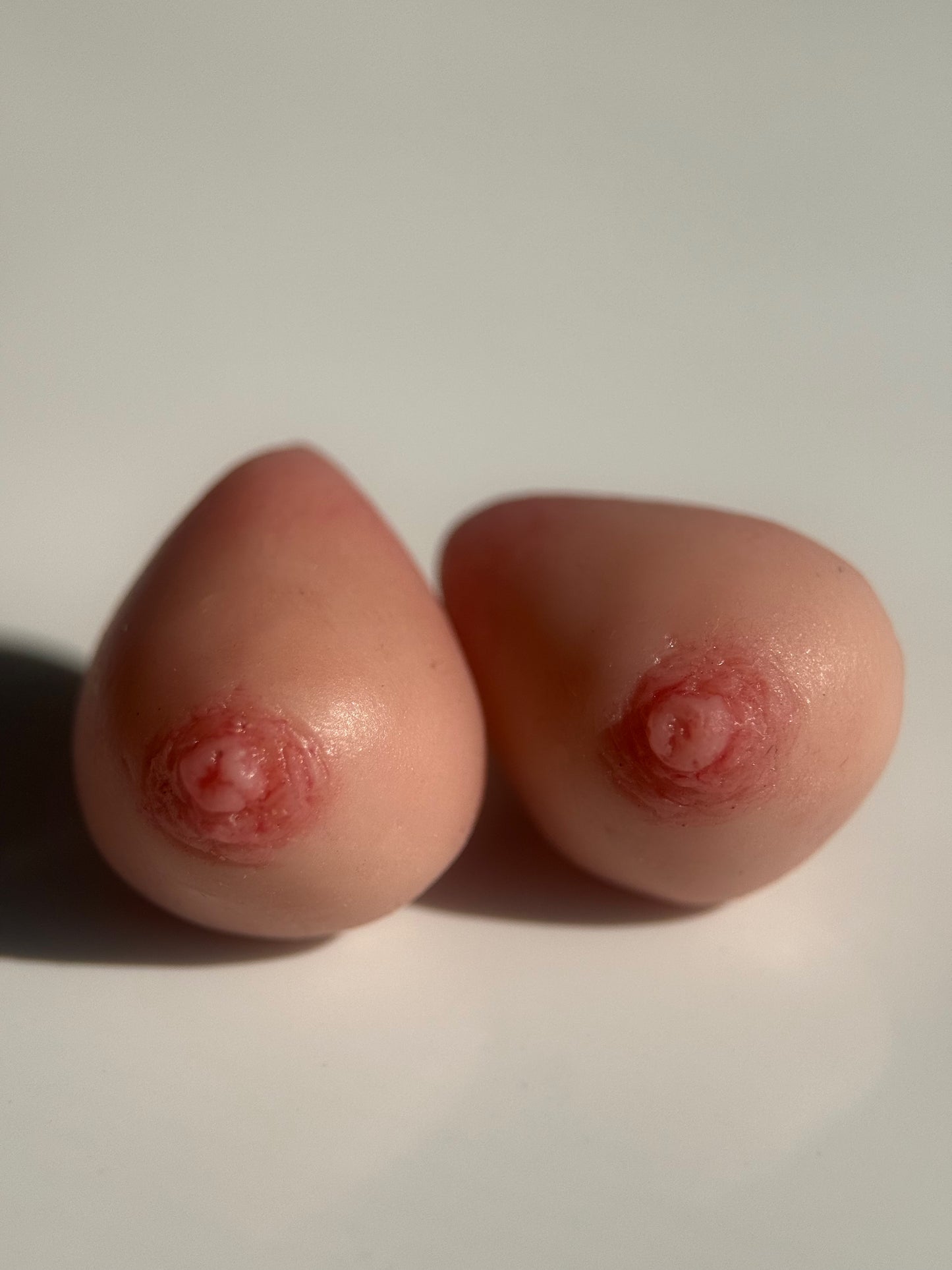 A pair of earrings that look like realistic caucasian breasts on a white background
