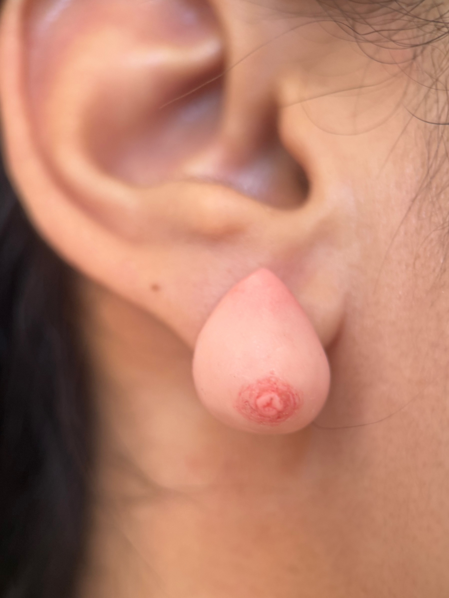 close up of an earring that looks like a realistic caucasian breast on an ear