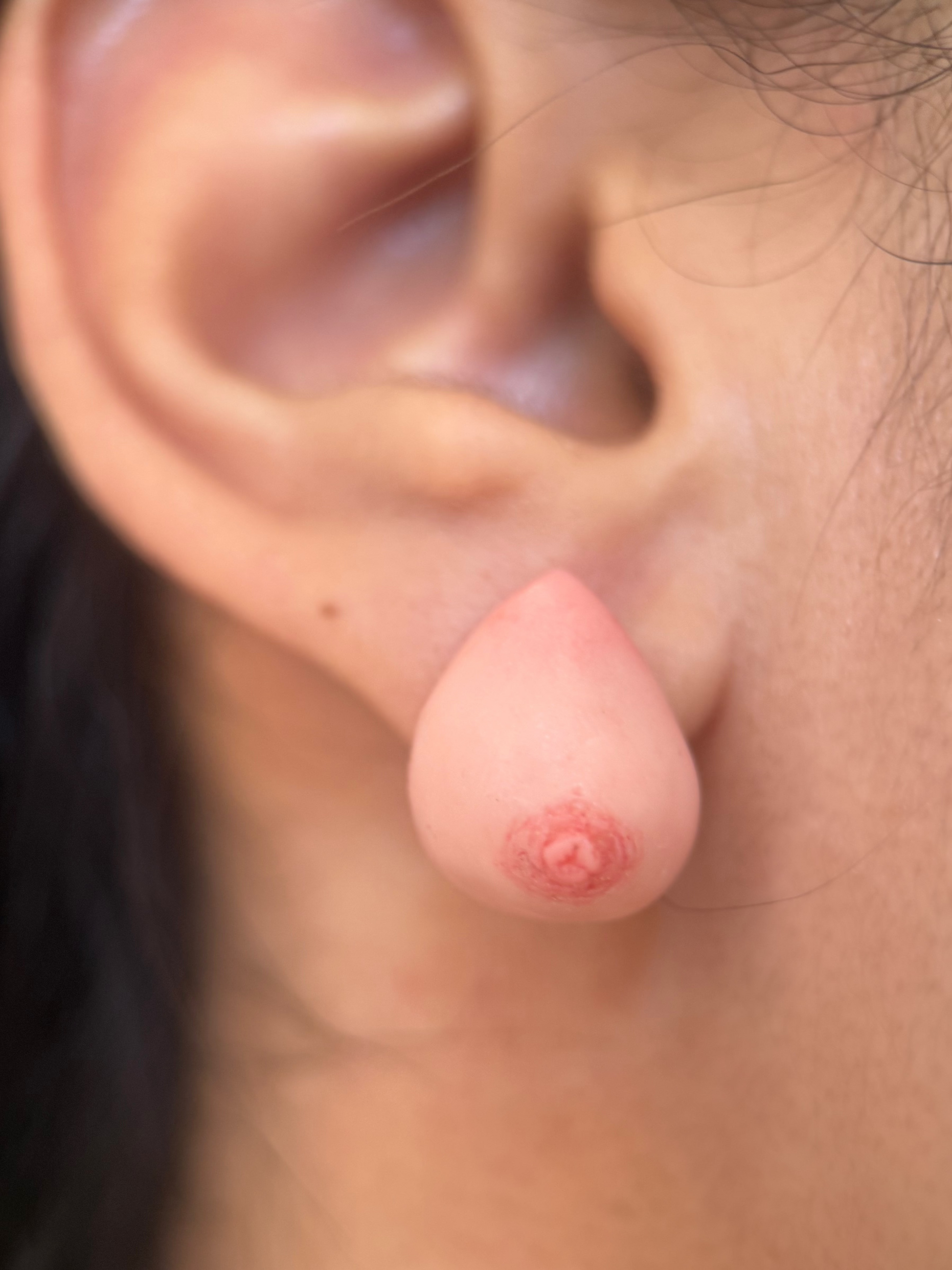 close up of an earring that looks like a realistic caucasian breast on an ear