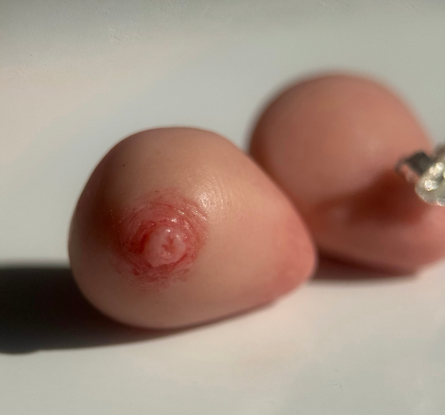 close up of an earring that looks like a realistic caucasian breast on a white background